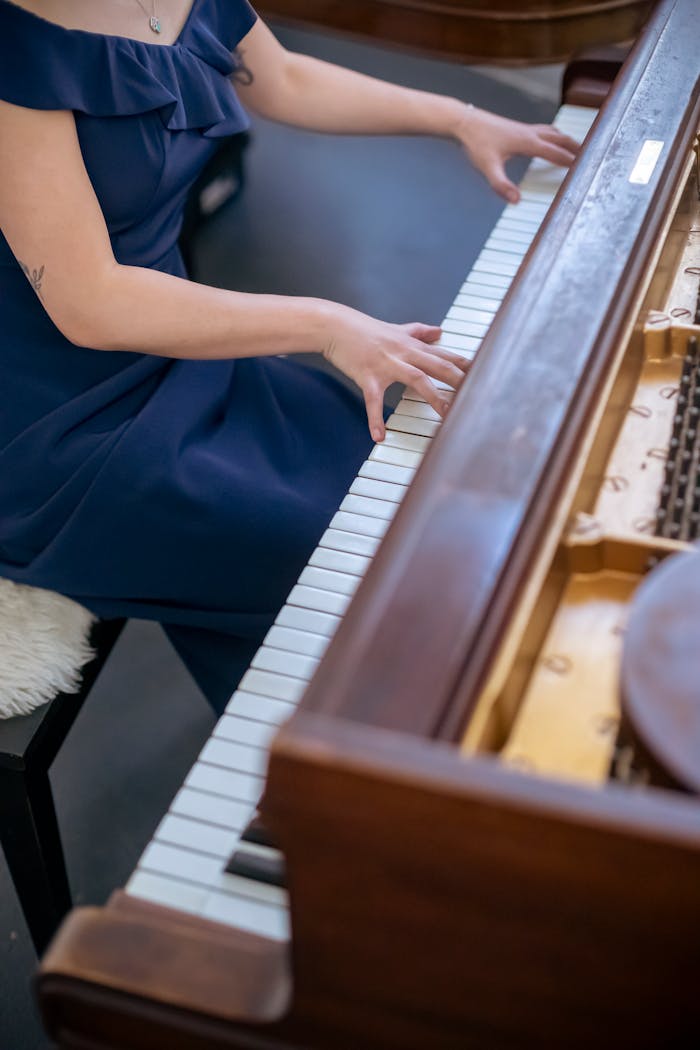 From above of faceless skilled female musician in stylish outfit playing melody on keyboard of piano while rehearsing in room